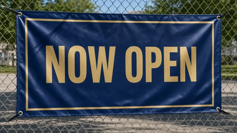Outdoor 'Now Open' vinyl banner hung on a fence